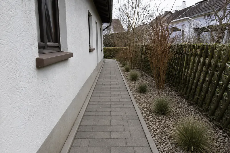 Derselbe Weg neu gepflastert mit grauem Betonstein und einem Kiesbeet daneben